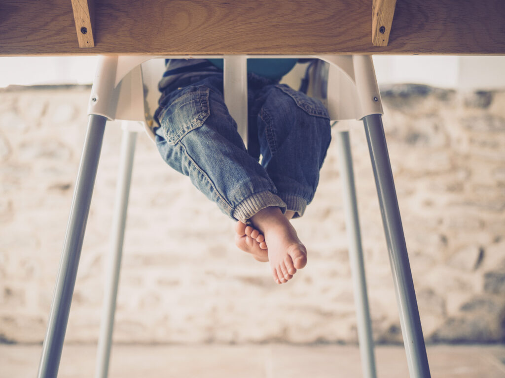 The legs of a toddler in a high chair at the table