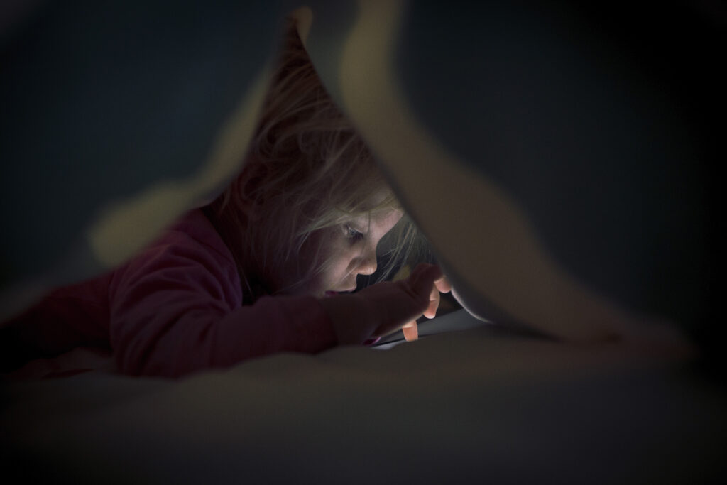 Little girl plays on mobile device under the duvet